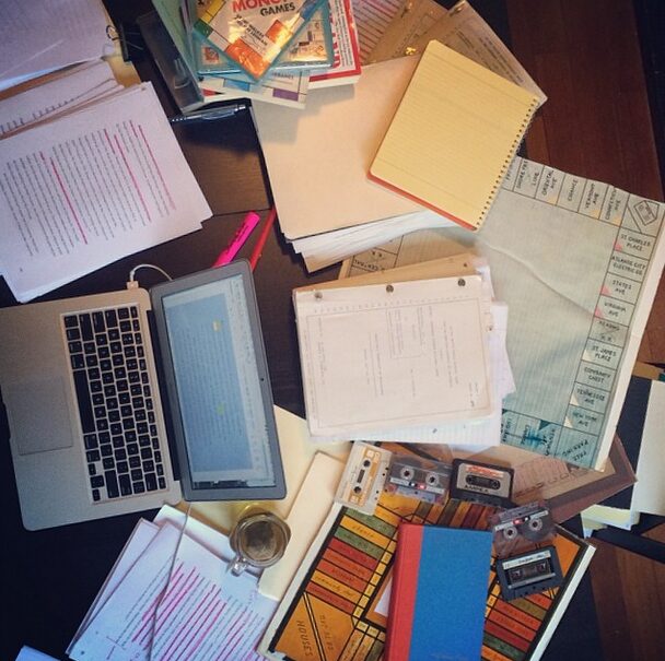 A desk covered with a laptop, notebooks, and archival research papers